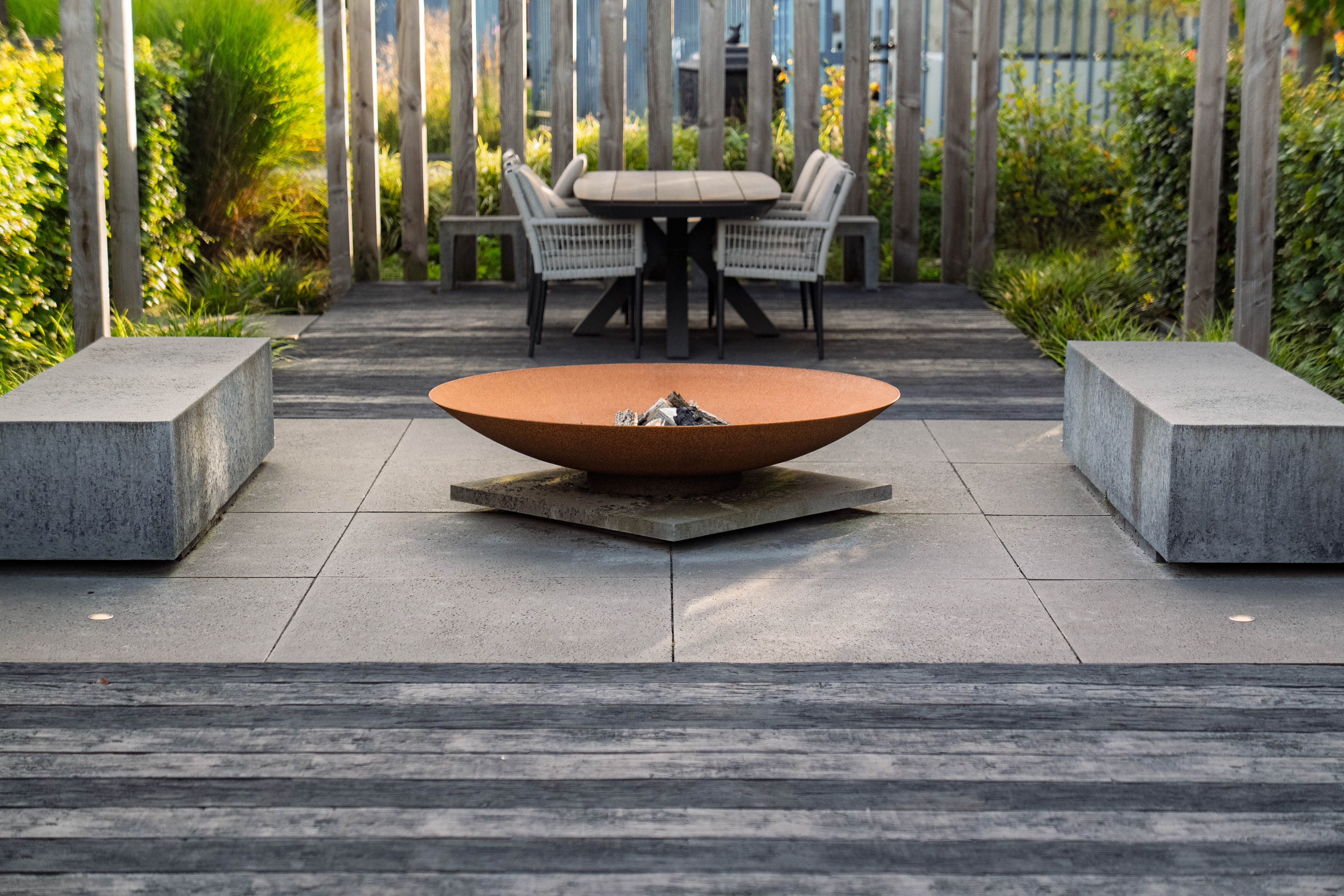 Outdoor patio with fire pit, chairs, and benches in a garden setting