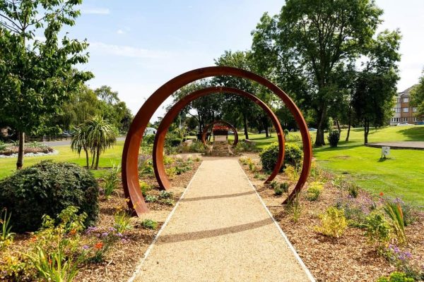 Garden pathway with large metal circular sculptures under a clear blue sky.