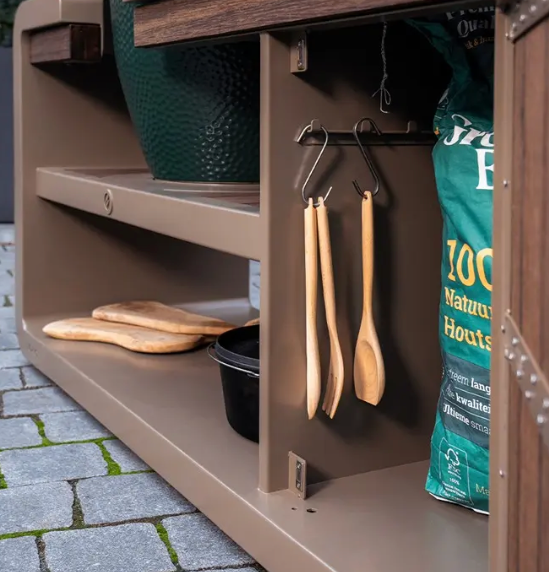 Outdoor kitchen setup with shelves, tools, and a bag on a stone patio.