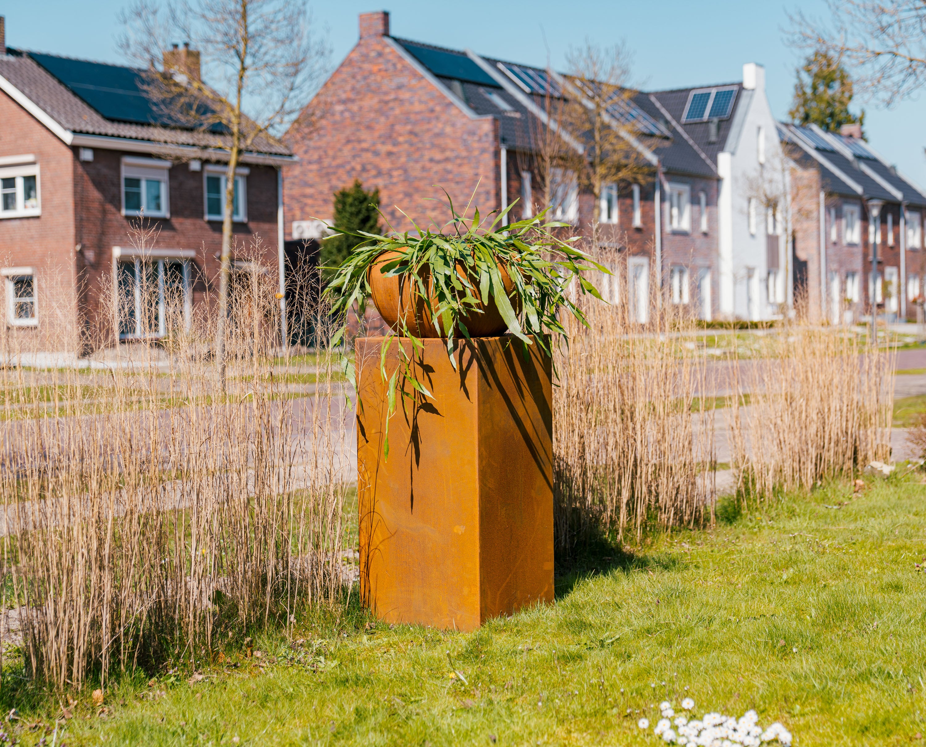 rust cououred pop on rust coloured plinth on grass in front of houses