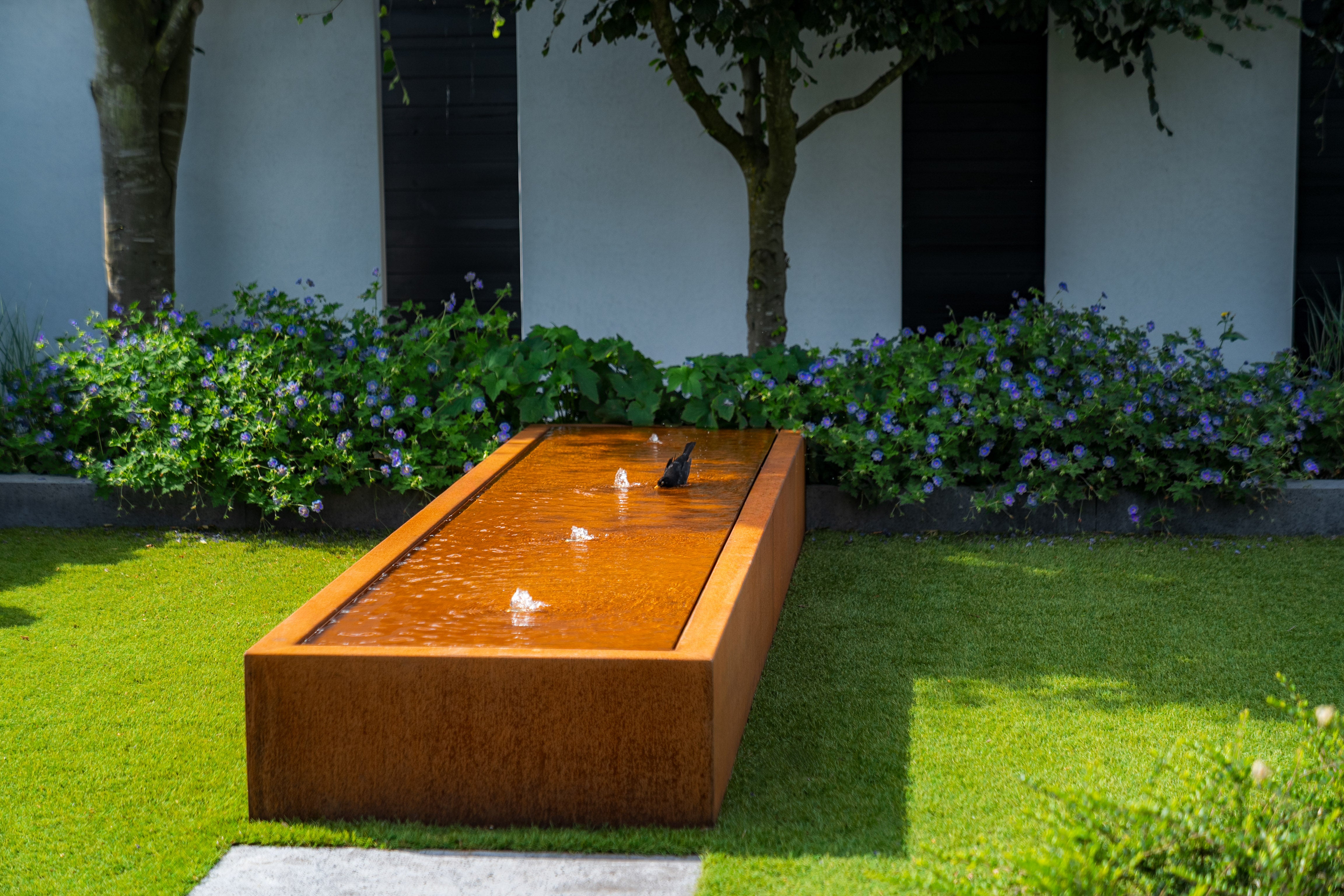 Wooden water feature in a garden with green grass and flowers