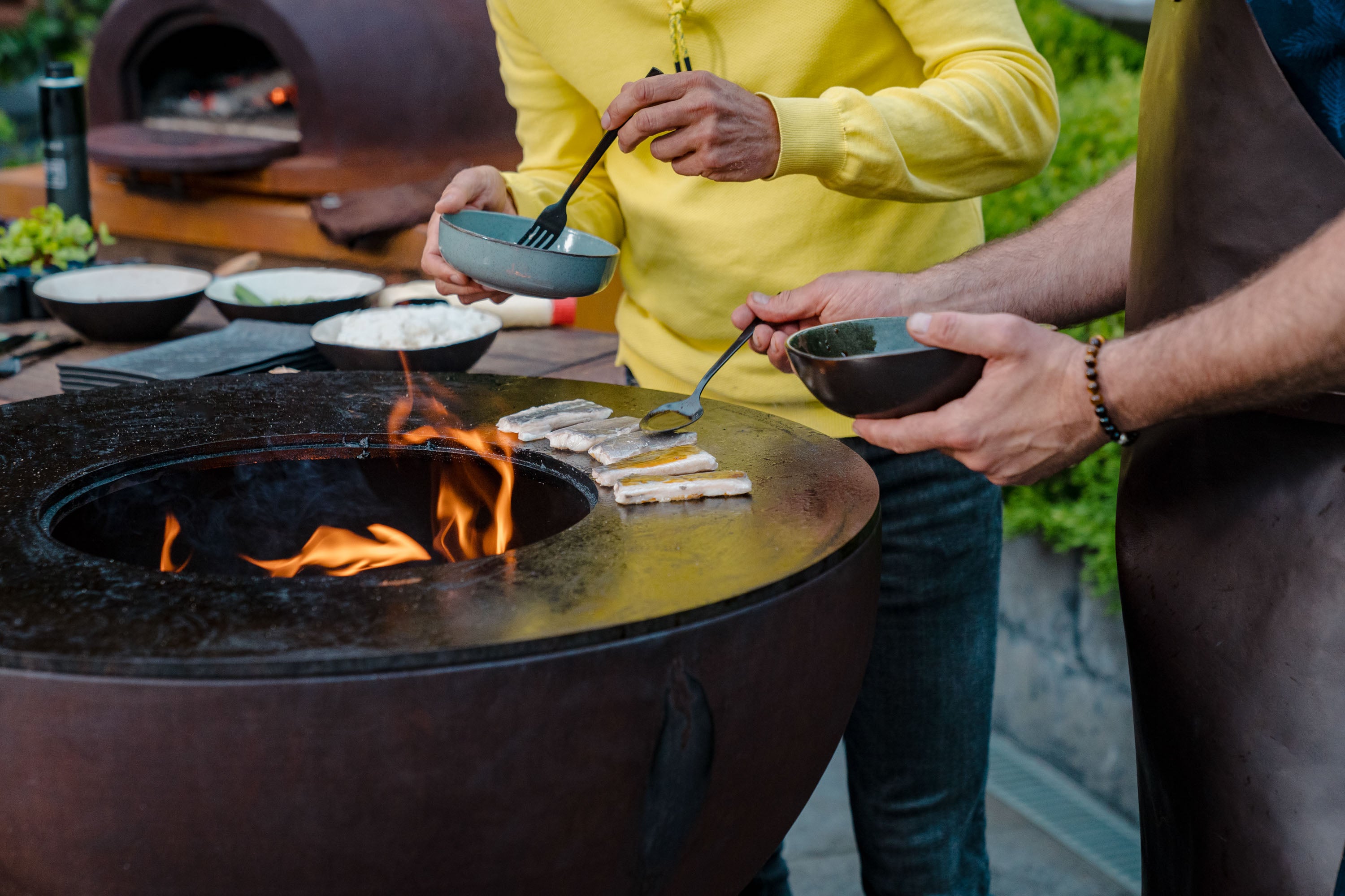 Two people eating from bowls by a fire pit outdoors