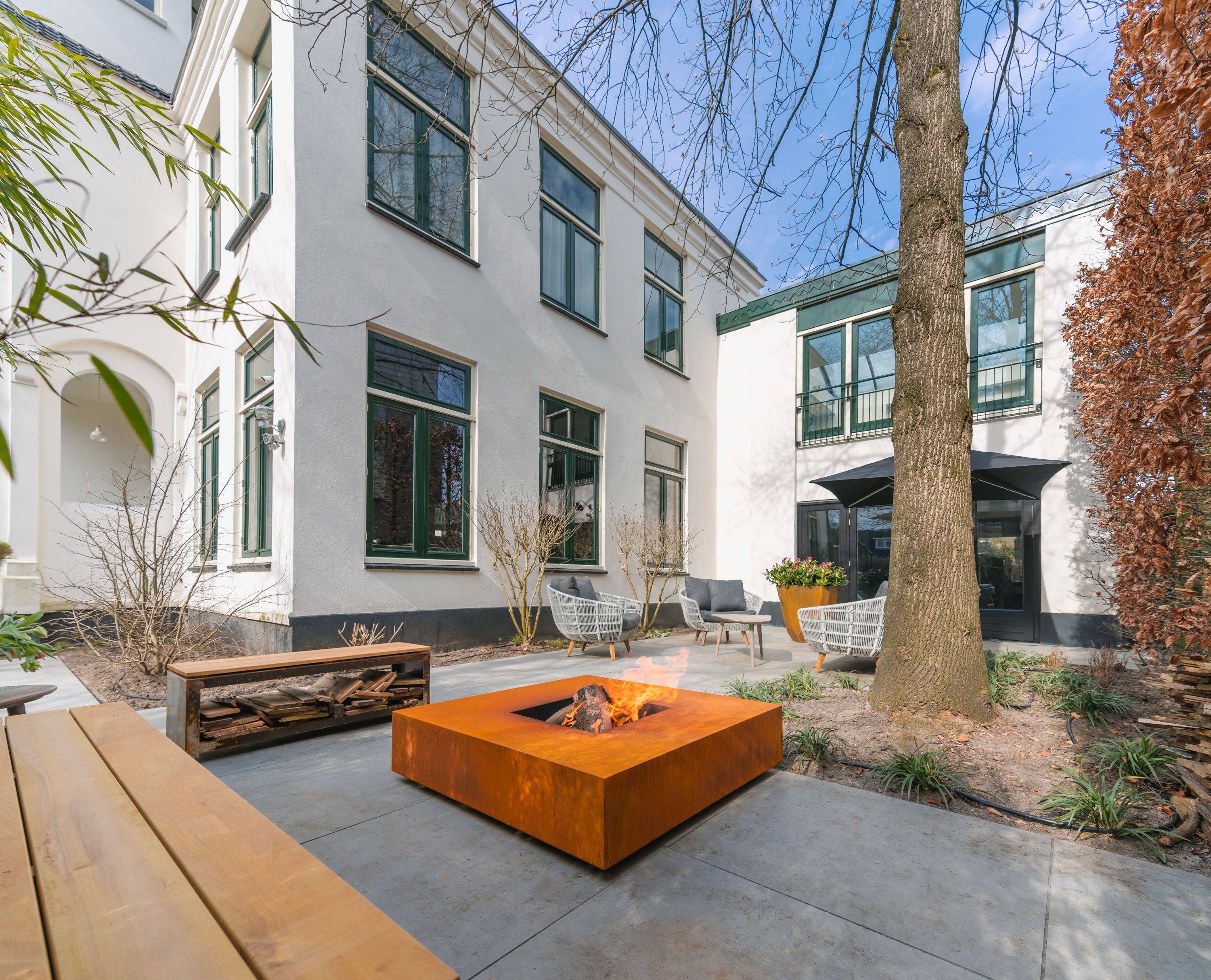 Outdoor patio area with a fire pit, benches, and a tree in an urban setting.