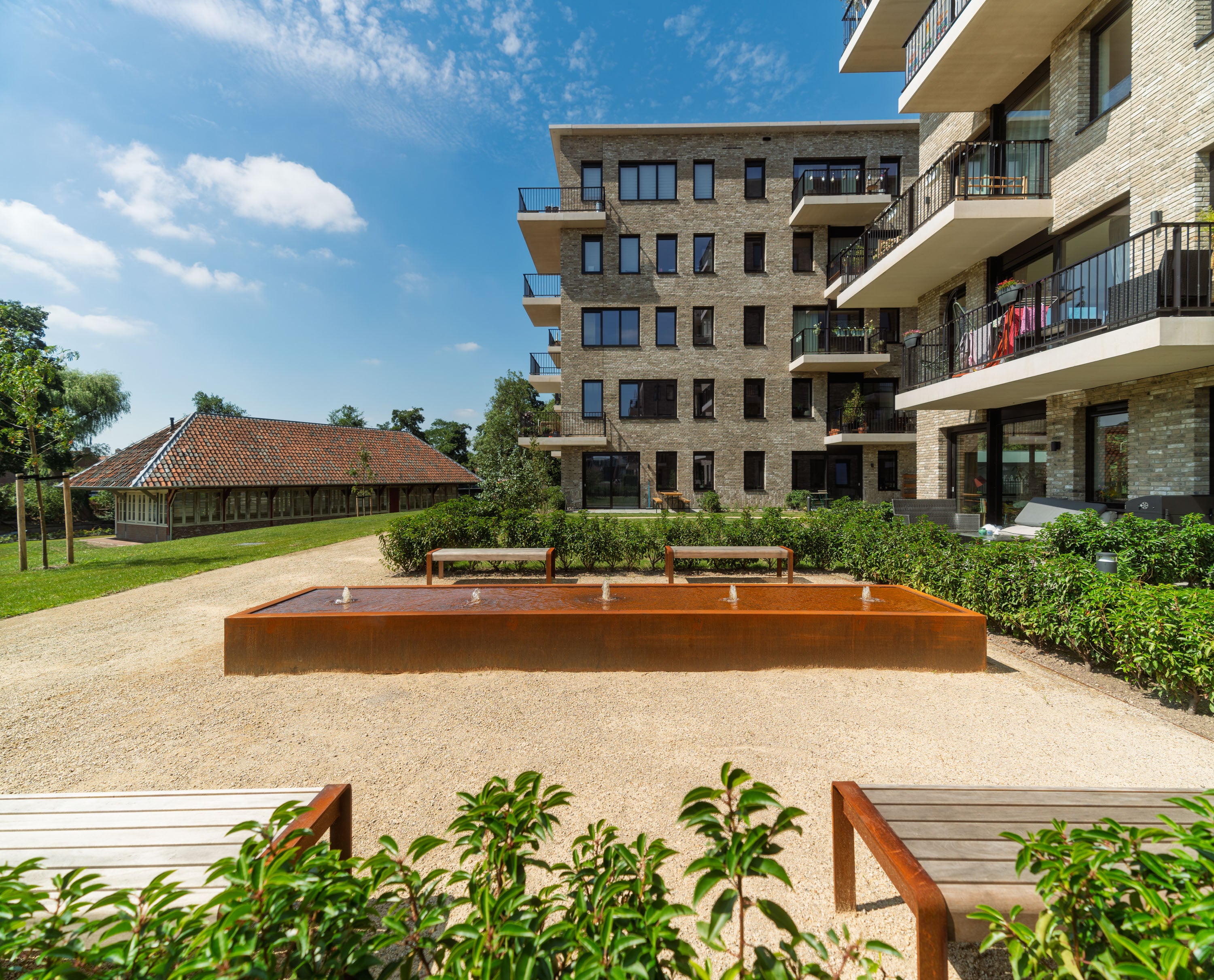 Modern apartment building with a courtyard featuring a metal sculpture and greenery.