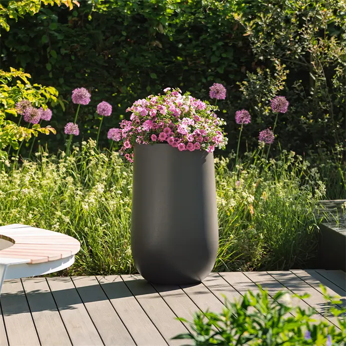 tall dark grey designer planter on decking planted with pink flowers 