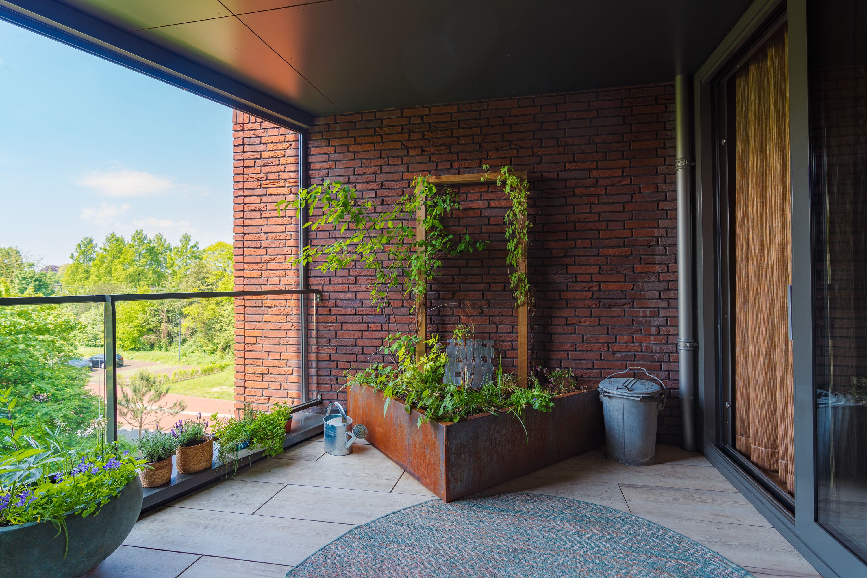 Balcony with brick wall, plants, and a view of trees. triangle planter with plants