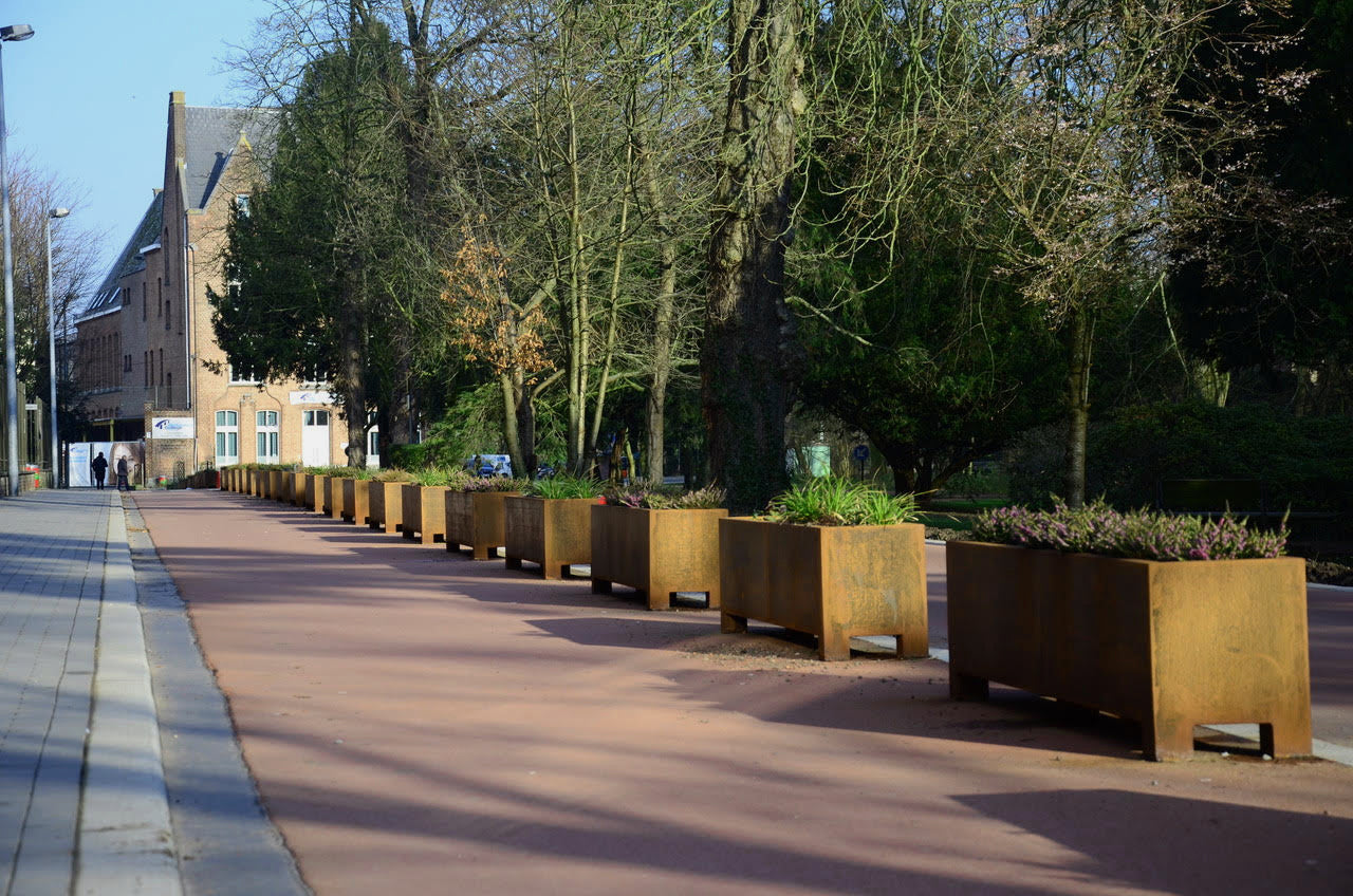 Row of metal planters with greenery along a sidewalk in an urban setting