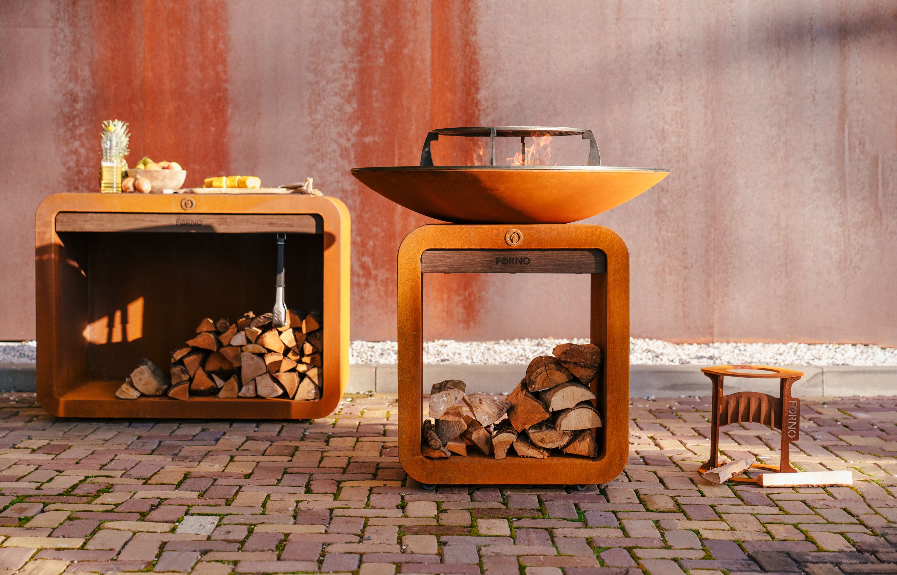 Outdoor fire pit with wood storage and a small table with items on a stone patio.