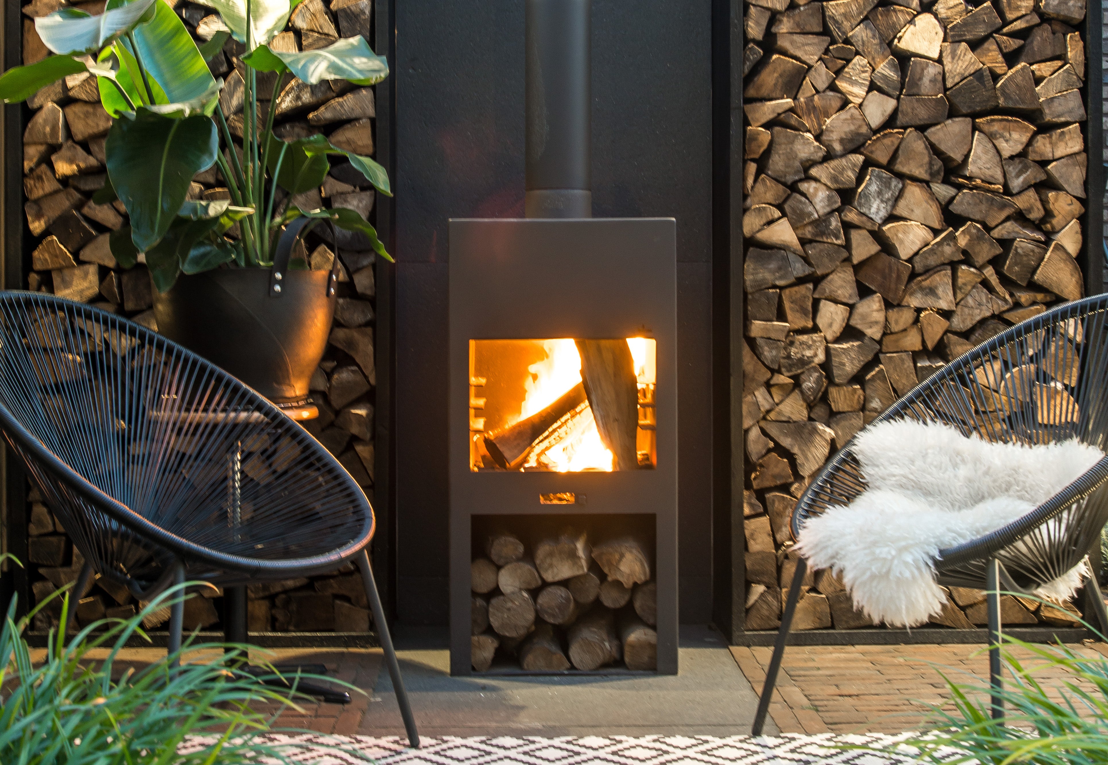 black outdoor stove surrounded by chairs and a wood store