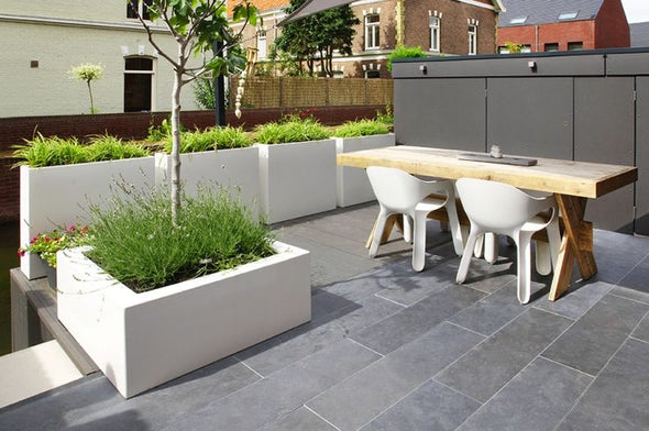 row of white fiberglass trough planters, planted with grasses,  situated on patio with table and chairs