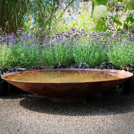 filled corten steel water bowl in front of flowers
