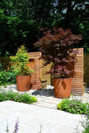 two round corten steel garden planters placed on gravel and planted with trees
