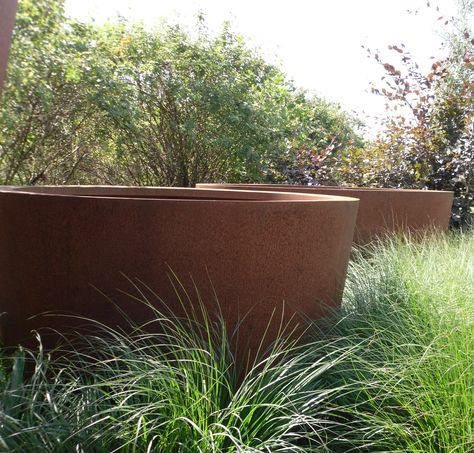 two large round corten steel garden planters situated in grass