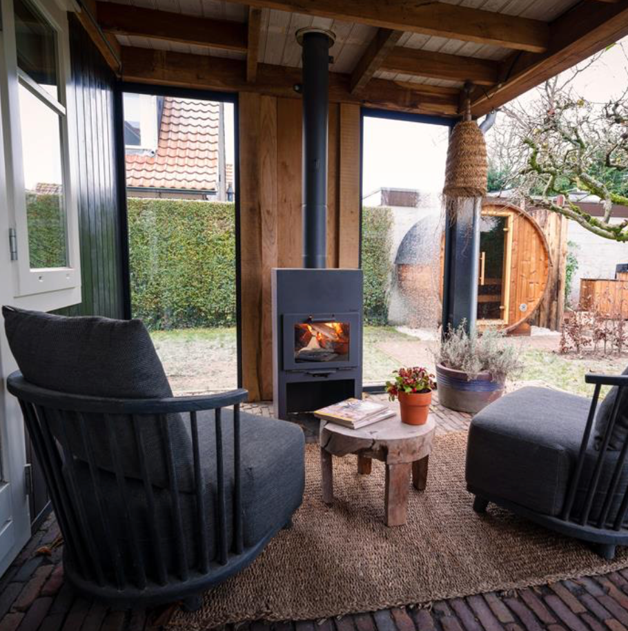 lit outdoor fireplace with flue, set under a porch with comfortable chairs either side