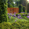 three corten screens with natural patterns set in mature garden