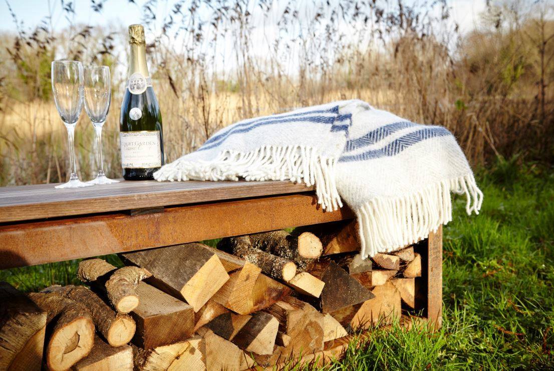rusted style wood storage bench in field with rug and wine bottle with glasses on top